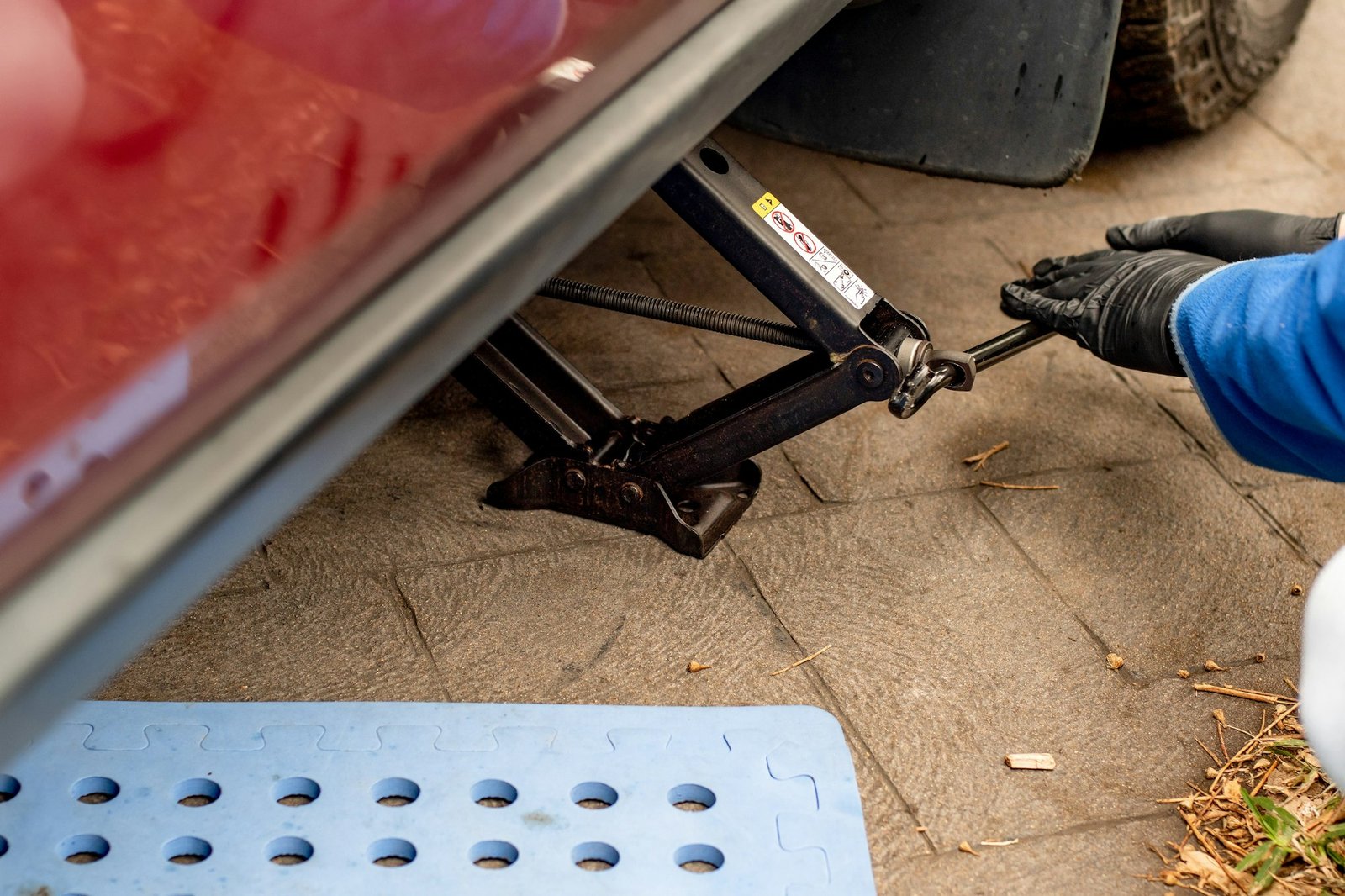 Garage Mechanic. A garage mechanic using scissors car jack to lift a car. DIY car vehicle repair